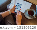 Managing personal finances on smartphone. No face woman checking financial balance on smartphone while enjoying a cup of tea at home. Financial documents, receipts on the table. focused on budgeting. 131506120