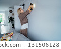 Side view middle aged woman in plaid shirt screwing a screw into the wall with electrical screwdriver. Woman wants to put a picture on the wall. Housekeeping work. Doing repair herself. DIY concept 131506128