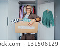 Smiling Woman with box of selected clothes from her wardrobe for donating to a Charity. Decluttering, Sorting clothes And Cleaning Up. Reuse, second-hand concept. Conscious consumer, sustainability. 131506129
