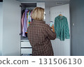 Middle aged Woman taking photo of shirt using smartphone for selling or donating her clothes. Decluttering , Sorting Clothes, And Cleaning Up wardrobe. Reuse, second-hand concept. Conscious consumer. 131506130