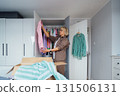 Middle aged woman selecting clothes from wardrobe for donating to Charity shop. Decluttering, Sorting clothes and Cleaning Up. Reuse, second-hand concept. Conscious consumer, sustainable lifestyle. 131506131