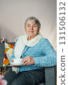 Smiling mature woman holding cup of tea, relaxing at home, positive senior female sitting on couch in modern living room looking satisfied feels good, older generation happy retired time enjoy life 131506132