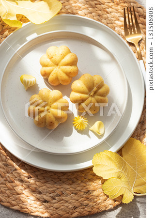 Pumpkin-Shaped Mini Cakes with Cream and Autumn Decor on Woven Placemat 131506908