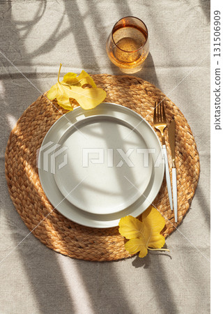 Table Setting with Yellow Leaves on White Plate and Woven Placemat under Sun Light Table Setting with Yellow Leaves on White Plate and Woven Placemat under Sun Light 131506909