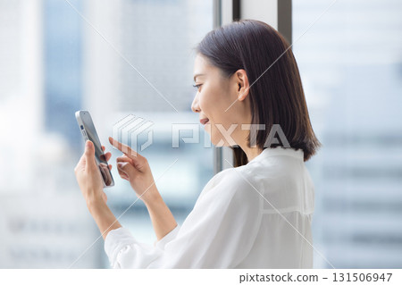 A young woman operating a smartphone by the window A young woman operating a smartphone by the window 131506947