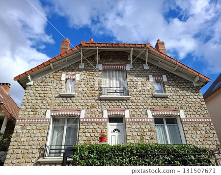 This cottage showcases a beautifully decorated facade with antique style and intricate natural stone trim. Bright flowers add color, enhancing its charming appeal against a clear blue sky. This cottage showcases a beautifully decorated facade with antique style and intricate natural stone trim. Bright flowers add color, enhancing its charming appeal against a clear blue sky. 131507671