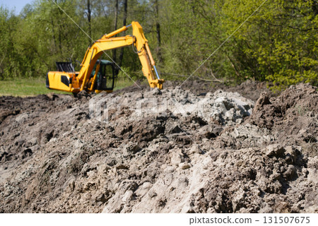 Big heap of soil with working excavator at the background at constructing new asphalt road at countryside near forest Big heap of soil with working excavator at the background at constructing new asphalt road at countryside near forest 131507675