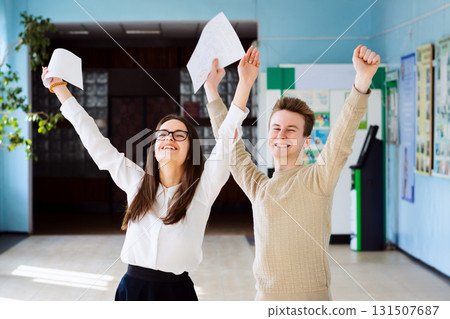 Two happy friends happy after researching their checked exams, raising hands up and expressing amusement of getting excellent grades for their work 131507687