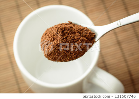 Spoon with ground coffee over the white empty cup against a brown bamboo background. Making coffee Spoon with ground coffee over the white empty cup against a brown bamboo background. Making coffee 131507746