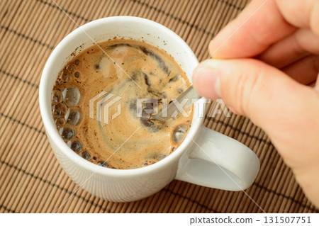 Man`s hand stirs coffee with a lot of foam with a spoon. Making coffee in the morning. Man`s hand stirs coffee with a lot of foam with a spoon. Making coffee in the morning. 131507751