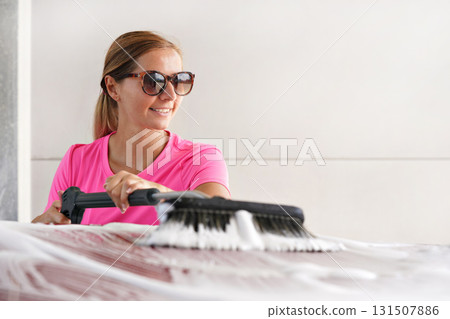 Young woman wearing pink t shirt and sunglasses cleaning her car in self serve carwash 131507886