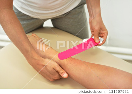 Young physiotherapist applying pink  kinesiology tape on female patient feet, closeup detail 131507921