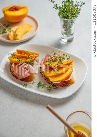 Toast with peach, cream cheese, ham and honey on a plate on a light background 131508075