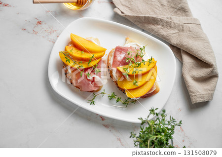 Toast with peach, cream cheese, ham and honey on a plate on a marble background Toast with peach, cream cheese, ham and honey on a plate on a marble background 131508079