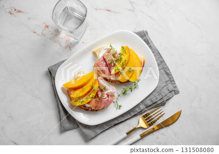 Toast with peach, cream cheese, ham and honey on a plate on a marble background 131508080