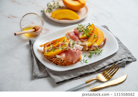 Bruschetta with peach, cream cheese, prosciutto and honey on a plate on a marble background Bruschetta with peach, cream cheese, prosciutto and honey on a plate on a marble background 131508082