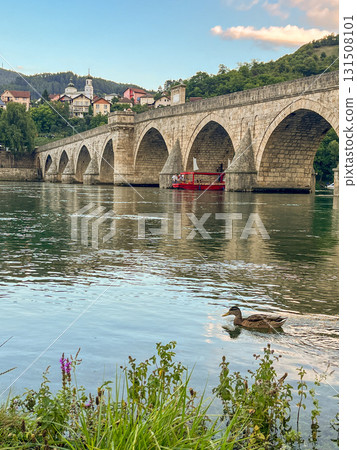 An ancient stone bridge with arches spanning the tranquil Drina River with wild flowers  131508101