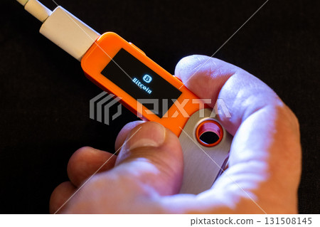 Adult man holding hardware wallet with Bitcoin indoors at night 131508145