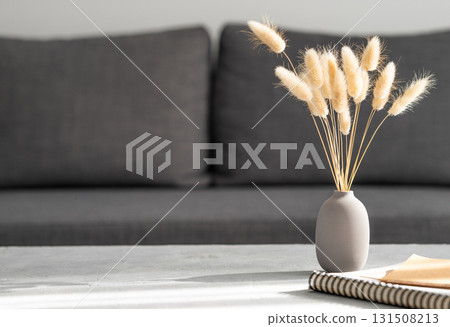 Vase with dried rabbit tail grass  and notebook on gray table in front of dark fabric sofa. 131508213