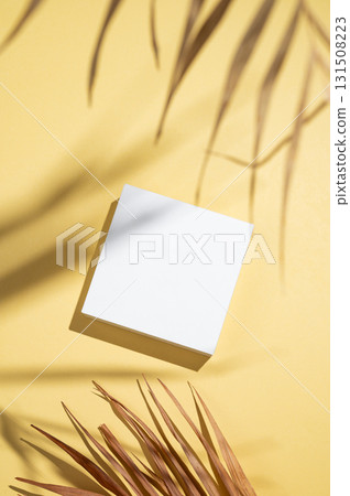 White box or podium on a yellow background with dry palm leaves and shadows. 131508223