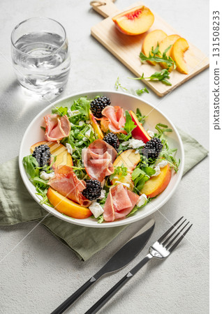 Fresh salad with peaches, arugula, feta, prosciutto and berries in a plate on a light background 131508233