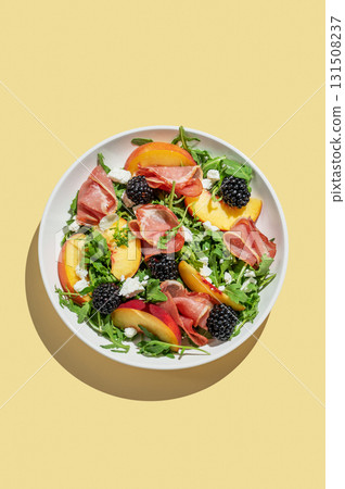 Fresh salad with peaches, arugula, feta, prosciutto and berries in a plate on a yellow isolated background 131508237