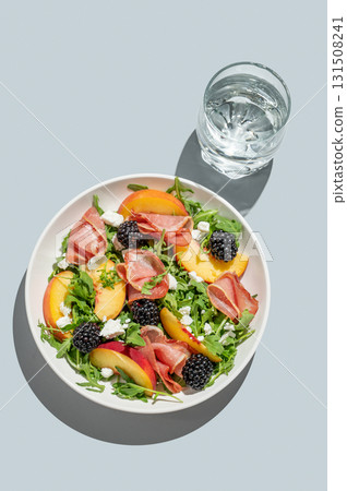 Salad with peaches, arugula, feta, prosciutto and berries in a plate on a blue background Salad with peaches, arugula, feta, prosciutto and berries in a plate on a blue background 131508241