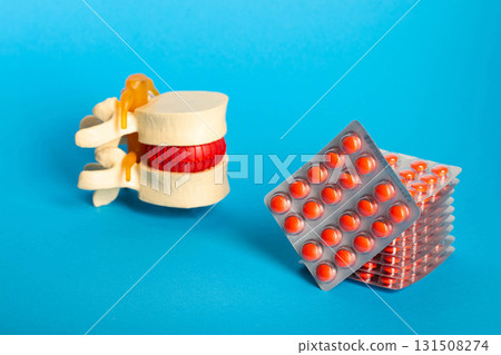 Stack of red pills on the background of the lumbar spine and blue background. Concept of homeopathic pills and chondroprotectors for the treatment of the back. Copy space for text, therapy Stack of red pills on the background of the lumbar spine and blue background. Concept of homeopathic pills and chondroprotectors for the treatment of the back. Copy space for text, therapy 131508274