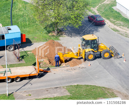 A yellow excavator dug up a road to lay electrical cables, workers stand near the hole, industry. Copy space for text 131508286