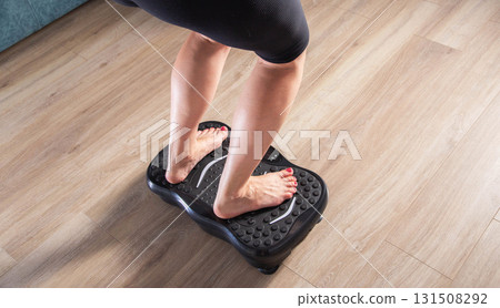 Women's legs stand on a sports vibration platform at home. Concept of doing sports at home. Modern home exercise machine, close-up Women's legs stand on a sports vibration platform at home. Concept of doing sports at home. Modern home exercise machine, close-up 131508292