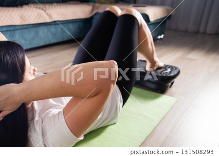 A young girl is doing sports on a vibration platform exercise machine at home in a home environment. The concept of getting rid of excess weight and cellulite. Sports device A young girl is doing sports on a vibration platform exercise machine at home in a home environment. The concept of getting rid of excess weight and cellulite. Sports device 131508293