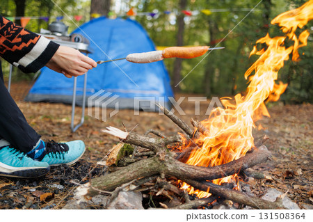 Close-up of sausages roasting over campfire with tent in background Close-up of sausages roasting over campfire with tent in background 131508364
