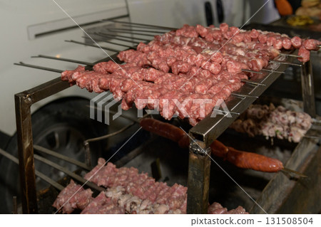 Juicy sausage skewers of raw meat sizzle ready to cooking on the grill 131508504