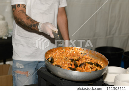 Chef prepares a large pan of seafood pasta featuring mussels at a culinary event during the evening Chef prepares a large pan of seafood pasta featuring mussels at a culinary event during the evening 131508511
