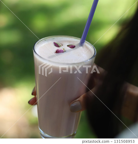 A person is holding a glass of pink liquid with a straw in it 131508953