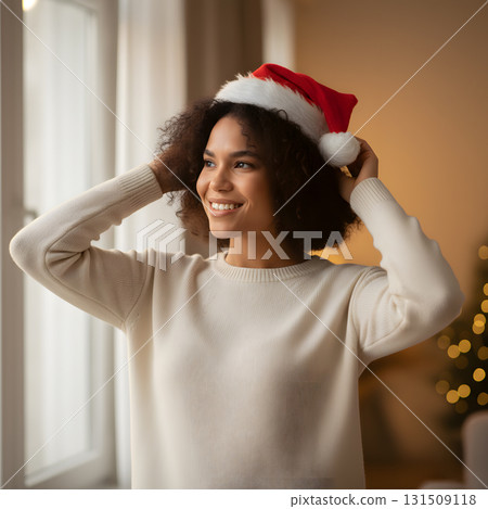 Smiling young woman adjusting a festive Santa hat indoors 131509118