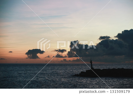 A tranquil coastal scene at dusk features a lone lighthouse on a rocky breakwater, 131509179
