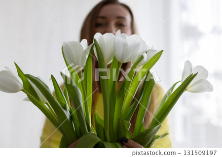 A young woman wearing yellow hoodie giving bouquet of white tulips. Spring mood. 131509197