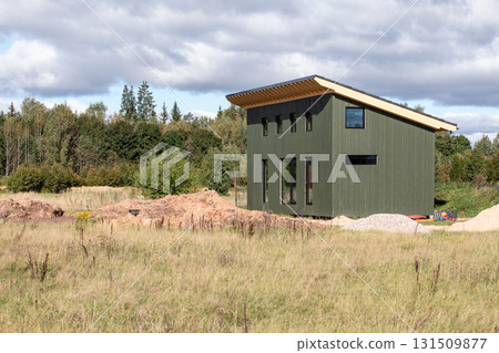 Modern small green wooden house under construction in a rural field with forest background 131509877