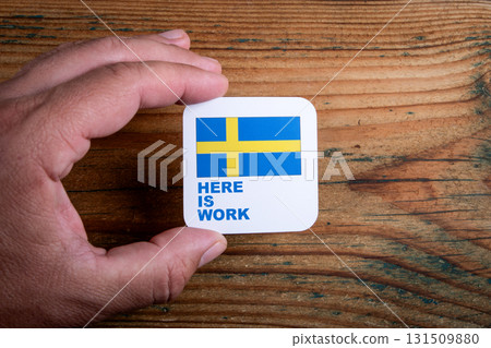 Hand holding a square card with the Swedish flag and the text Here Is Work. Employment opportunities Hand holding a square card with the Swedish flag and the text Here Is Work. Employment opportunities 131509880