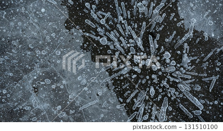 An abstract overhead perspective reveals delicate ice formations and trapped air bubbles emerging from a dark, fractured surface, creating a dynamic, intricate pattern. 131510100