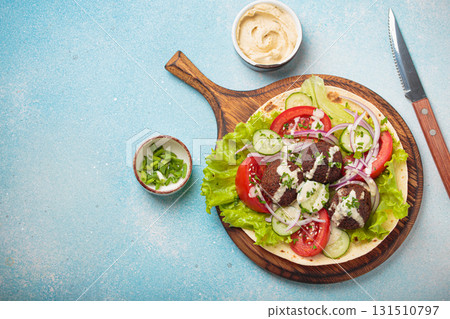 Preparing and cooking falafel wrap on pita on wooden cutting board with hummus top view light blue background, space for text 131510797