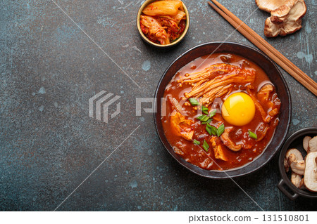 Traditional Korean kimchi jjigae hot soup or stew with egg yolk in black rustic bowl on dark background top view, space for text 131510801