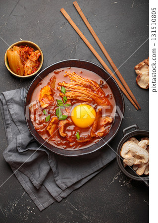 Traditional Korean kimchi jjigae hot soup or stew with egg yolk in black rustic bowl on dark background top view 131510805
