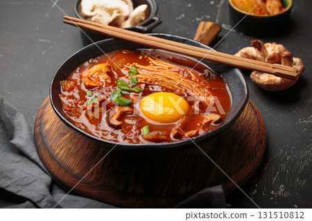 Traditional Korean kimchi jjigae hot soup or stew with egg yolk in black rustic bowl on dark background top view 131510812