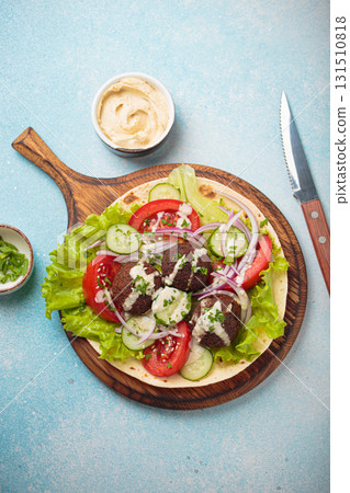 Preparing and cooking falafel wrap on pita on wooden cutting board with hummus top view light blue background Preparing and cooking falafel wrap on pita on wooden cutting board with hummus top view light blue background 131510818