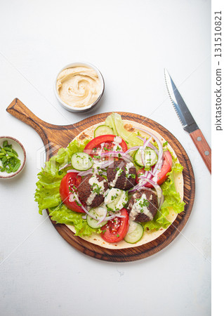 Preparing and cooking falafel wrap on pita on wooden cutting board with hummus top view white background 131510821