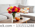 Autumn, fall cozy mood composition for hygge home decor. Bouquet of fresh multicolor dahlia flowers, small pumpkin, burning candles on the coffee table in modern living room. Selective focus. 131511288