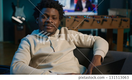 Smiling male freelancer browsing the web on laptop in a modern apartment, demonstrating a lifestyle of independence. Productivity in a virtual workspace, man multitasking. Camera A. 131513063