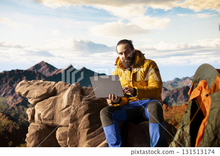 Nature lover workaholic always connected to the internet and scrolling on laptop, enjoying web strong signal on a mountain top with a breathtaking landscape. Uninterrupted work. 131513174